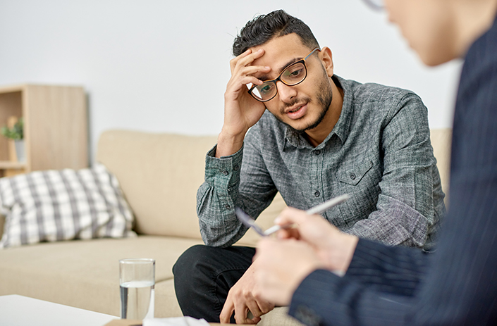 Man with glasses speaking to psychologist who is writing down notes