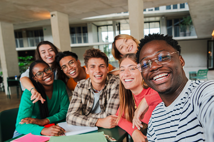 A group of diverse young adults smiling and posing together in a casual setting, capturing a joyful moment of friendship and collaboration.